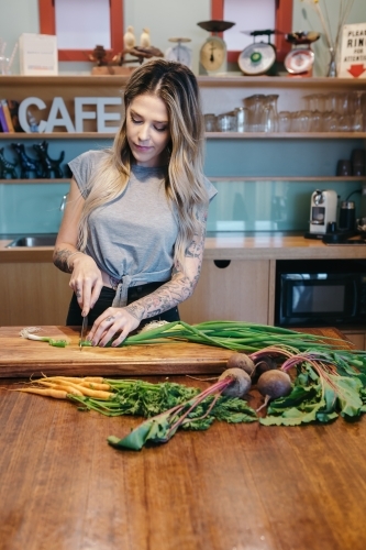 Young woman chopping veggies at home in the kitchen - Australian Stock Image