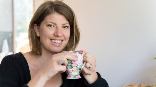 Young woman holding teacup smiling - Australian Stock Image