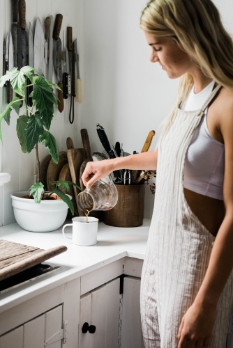 Young woman in overalls pouring herself a coffee at the kitchen bench