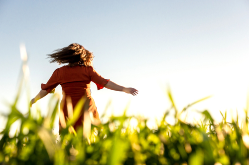 Young woman in red dress twirling in a green field - Australian Stock Image
