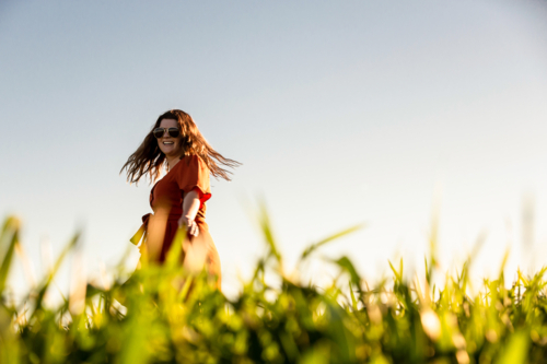 Young woman in red dress twirling in a green field - Australian Stock Image