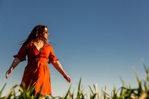 Young woman in red dress twirling in a green field - Australian Stock Image