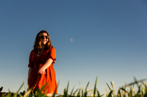 Young woman in red dress twirling in a green field - Australian Stock Image