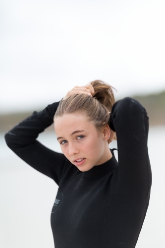 Young woman in wetsuit tying hair back - Australian Stock Image
