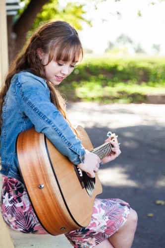 Young woman looking down playing guitar outside - Australian Stock Image