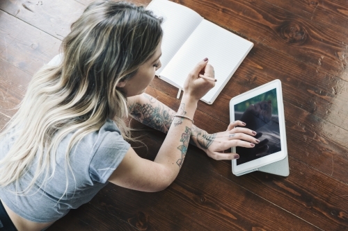 Young woman lying on the floor studying and browsing the internet on a tablet - Australian Stock Image