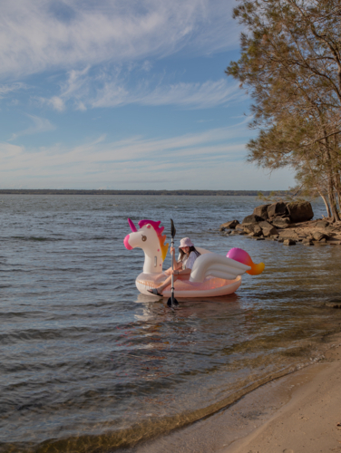 Young woman on a blow up unicorn on water - Australian Stock Image