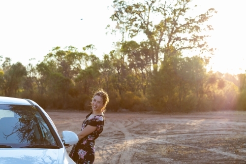 young woman opening passenger door of car in rural setting with sun flare - Australian Stock Image