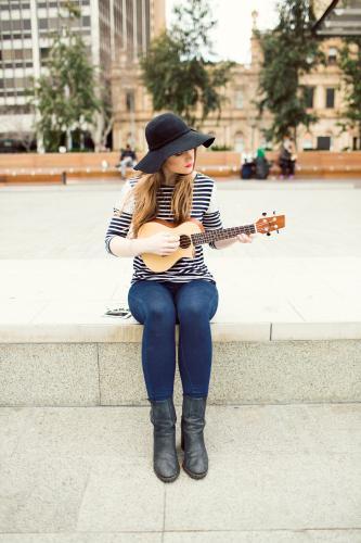 Young woman playing a ukulele on city street - Australian Stock Image