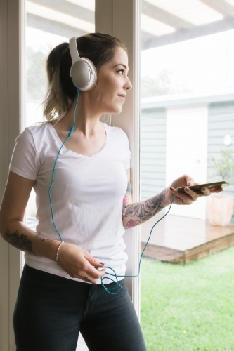 Young woman playing music on her phone looking out the window - Australian Stock Image