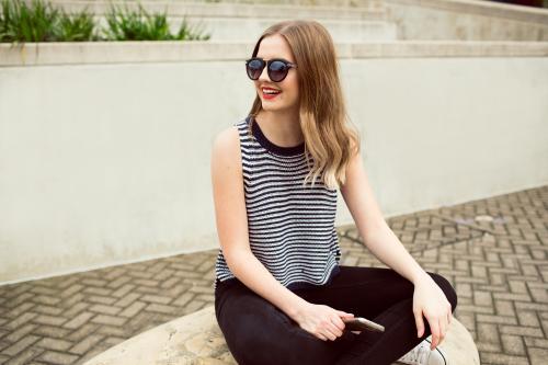 Young woman sitting against a wall with a phone and sunglasses
