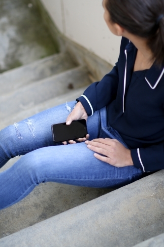 Young woman sitting in stairwell holding mobile phone