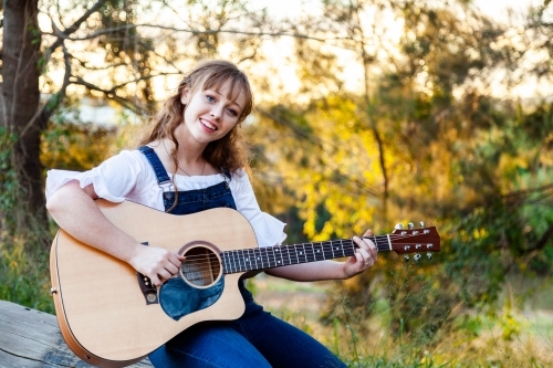 Young woman sitting on log playing instrument - Australian Stock Image