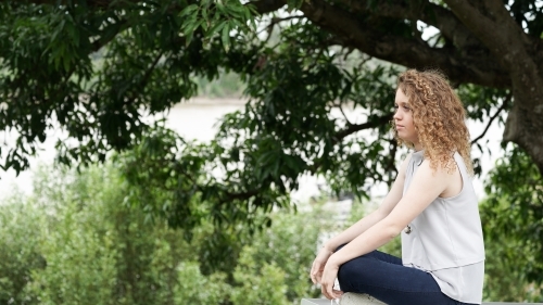 Young woman sitting on park table looking away - Australian Stock Image