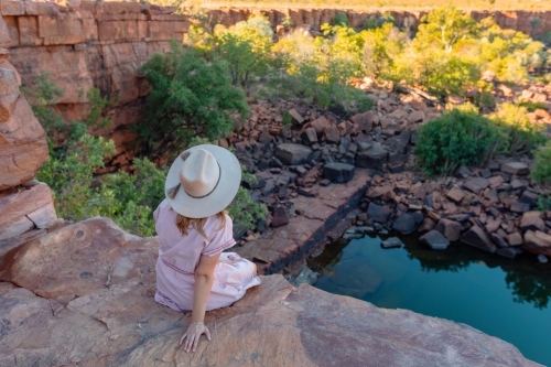 young woman sitting on rock ledge overlooking waterhole in the kimberley - Australian Stock Image