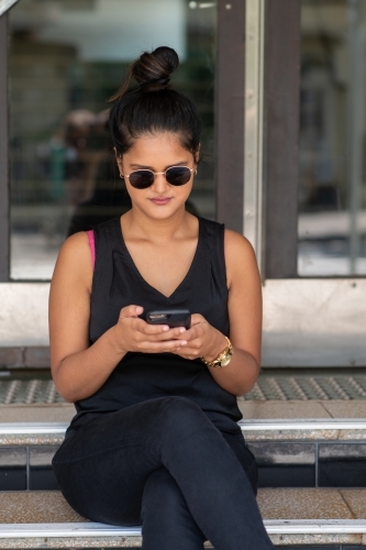 young woman sitting on stairs using phone - Australian Stock Image