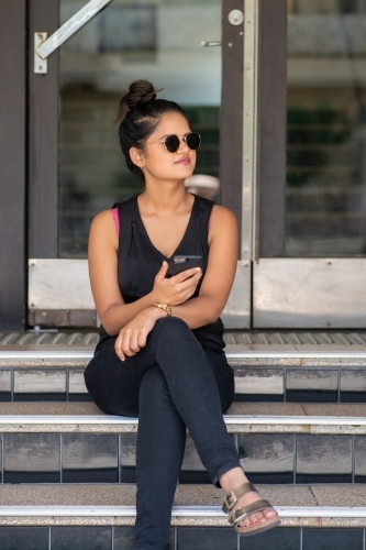 young woman sitting on stairs using phone - Australian Stock Image