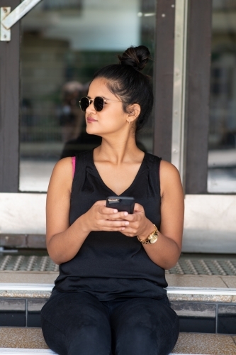 young woman sitting on stairs using phone - Australian Stock Image