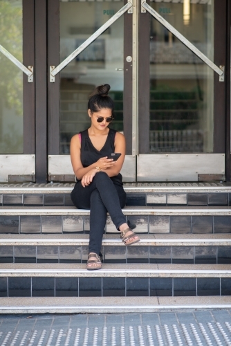young woman sitting on stairs using phone