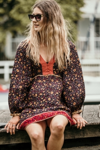 Young woman sitting outdoors wearing sunglasses. - Australian Stock Image