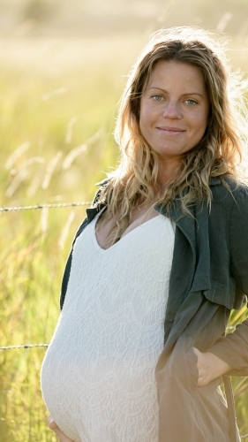 Young woman standing in field with sunflare behind, looking at camera