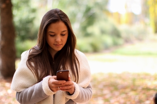Young woman standing in front of a group of friends using a mobile phone - Australian Stock Image