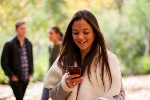 Young woman standing in front of a group of friends using a mobile phone - Australian Stock Image