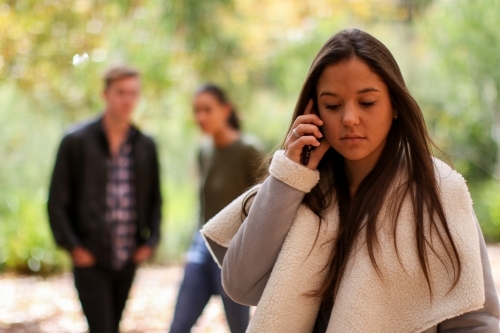 Young woman standing in front of a group of friends using a mobile phone - Australian Stock Image