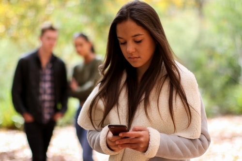 Young woman standing in front of a group of friends using a mobile phone