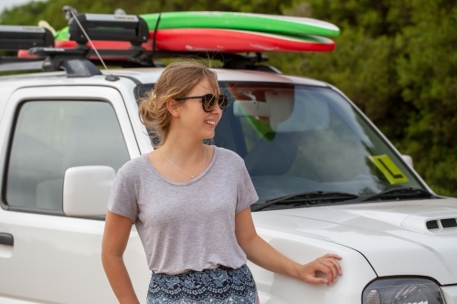 Young woman standing near vehicle with surfboards on roof