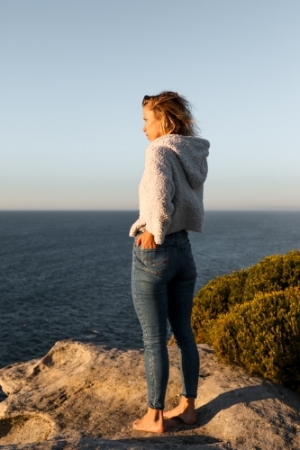 Young woman standing on coastal clifftop at sunrise looking out to sea