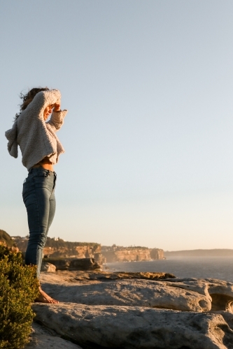 Young woman standing on coastal clifftop at sunrise looking out to sea