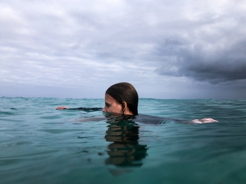 Young woman swimming in ocean on overcast day - Australian Stock Image