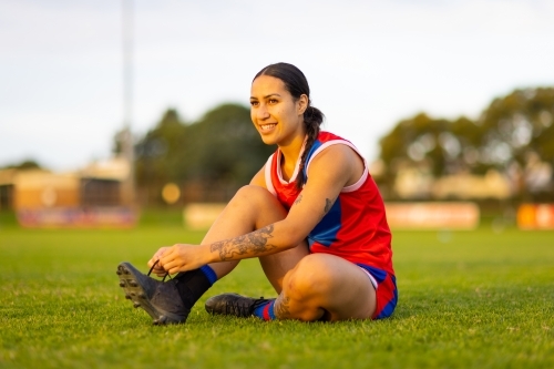 young woman tying football boot on playing field