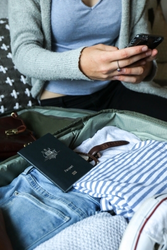 Young woman using her phone next to her packed bag ready to travel - Australian Stock Image