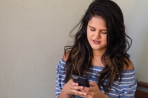 young woman using mobile phone at a bus stop - Australian Stock Image