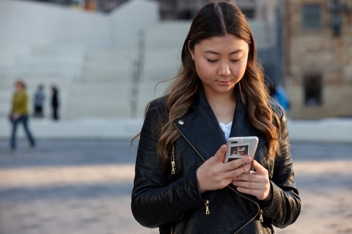 Young woman using mobile phone wearing leather jacket - Australian Stock Image