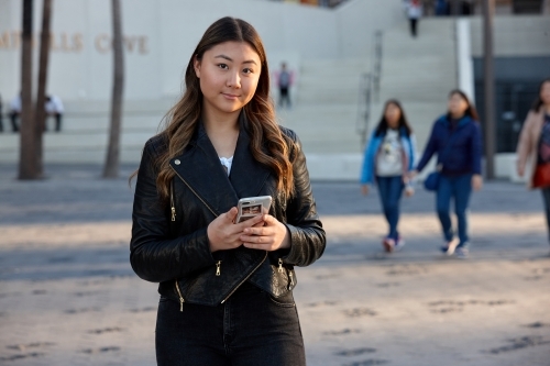 Young woman using mobile phone wearing leather jacket - Australian Stock Image