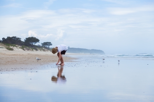 Young woman walking along beachcombing looking for shells at the seaside - Australian Stock Image