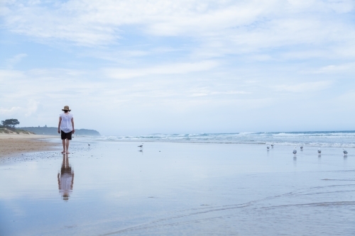 Young woman walking along beachcombing looking for shells at the seaside - Australian Stock Image