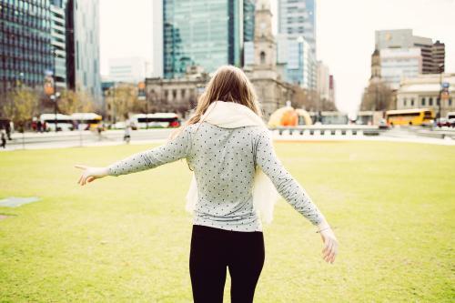 Young woman walking away on grass in the city