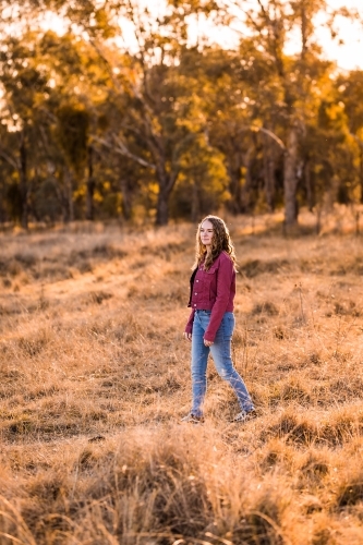 Young woman walking through paddock in golden light - Australian Stock Image