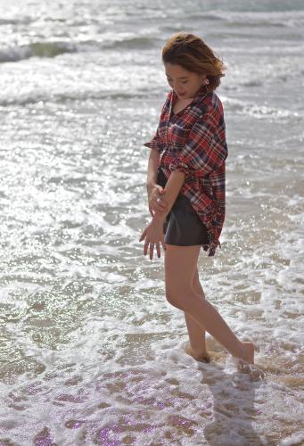 Young woman walking through the shallow waves on the beach - Australian Stock Image