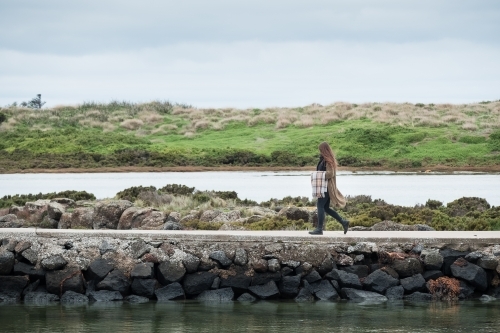 Young woman walks on jetty by the river.