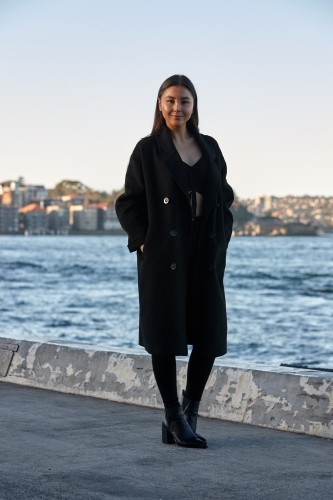 Young woman wearing coat by harbour - Australian Stock Image