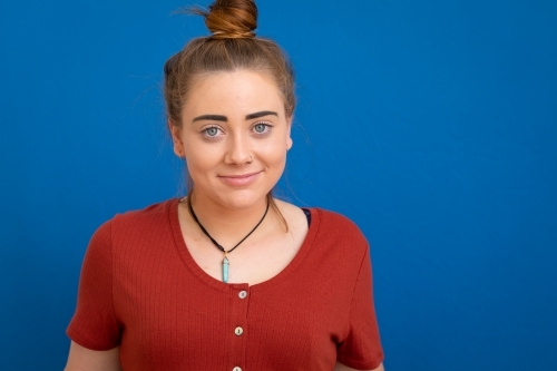 young woman with bun standing against blue background - Australian Stock Image