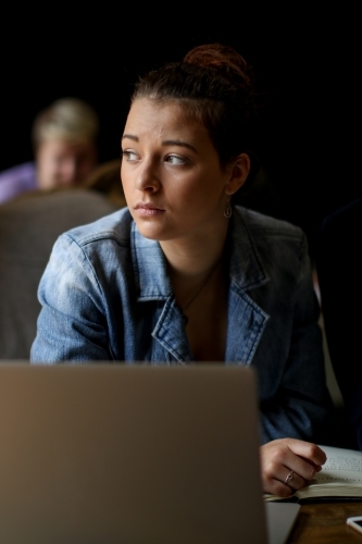 Young woman with concerned expression sitting at a desk behind a laptop