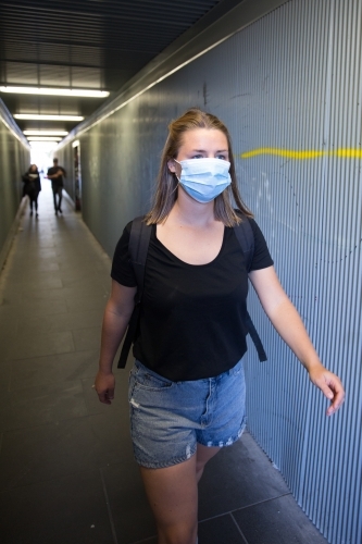 Young Woman with Face Mask Walking Through City Tunnel - Australian Stock Image