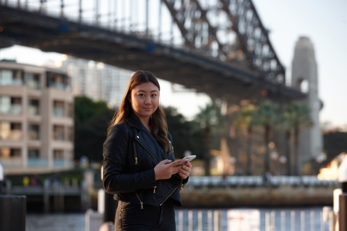 Young woman with mobile phone in front of harbour bridge - Australian Stock Image