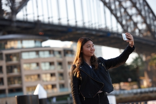 Young woman with mobile phone in front of harbour bridge - Australian Stock Image